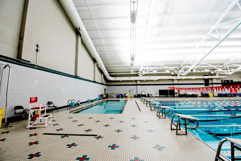 The smaller pool at the far end of the deck beside a row of starting blocks and a lifeguard chair