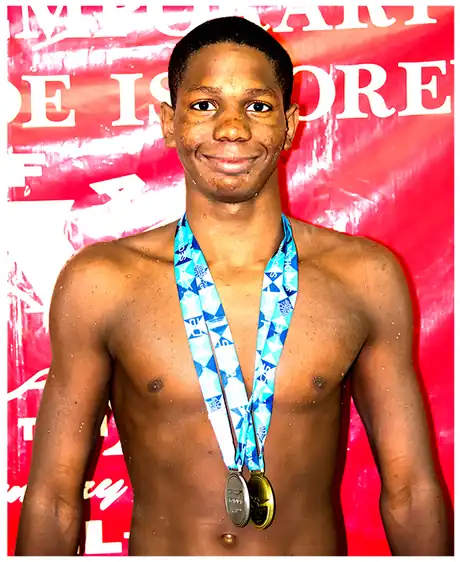 A Dolphins swimmer wearing his medals in front of a red team backdrop