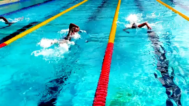 Two freestyle swimmers racing down lanes marked by red and yellow lane ropes