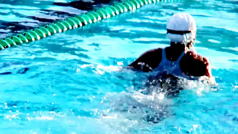 A swimmer in a white cap breathing to the side beside a green lane rope