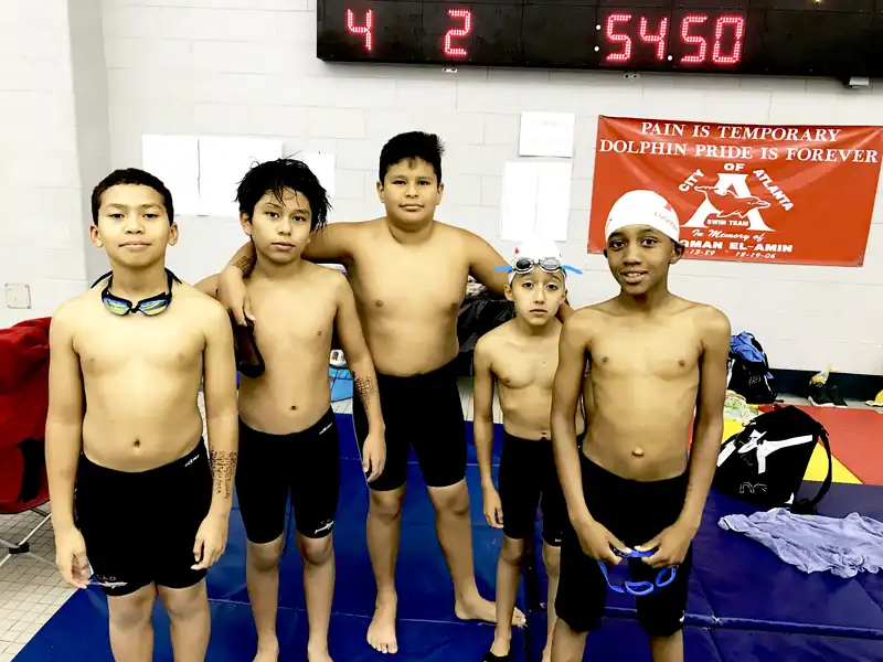 Five young Dolphins in goggles under the scoreboard and the team banner