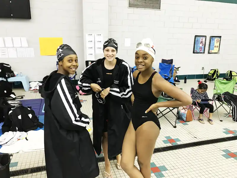 Three Dolphins swimmers in team parkas and caps on the pool deck at a meet