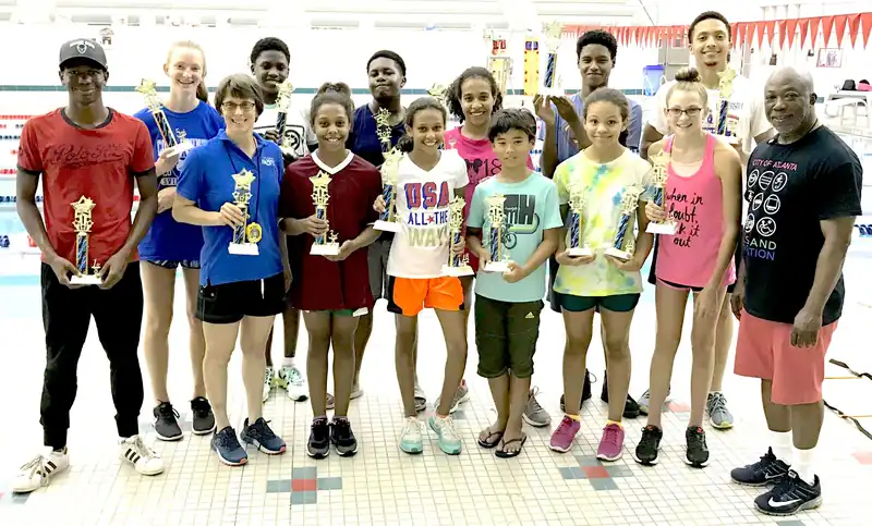 Dolphins swimmers holding trophies with their coach at a meet